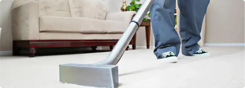 Carpet cleaning technician using a hot-water extraction wand on a light-colored carpet in a living room, Bellevue, WA.