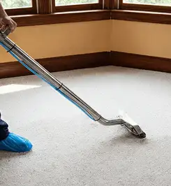 Steam carpet cleaning technician using a hot-water extraction wand on a residential carpet, wearing blue protective shoe covers Bellevue, WA.